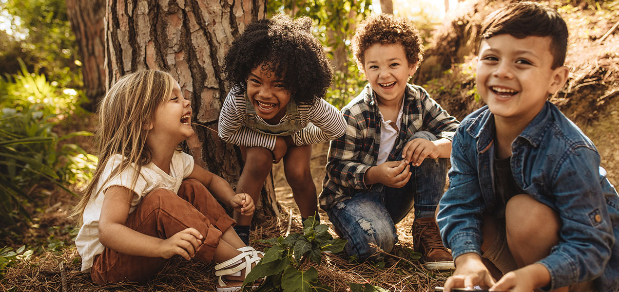 Groupe d’enfants divers souriants assis ensemble dans la forêt et regardant la caméra.