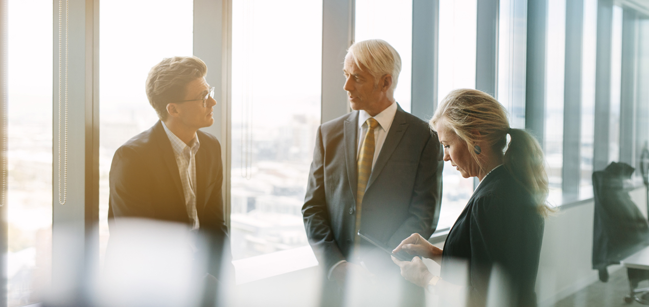 Three business colleagues standing behind the glass and discussing work.