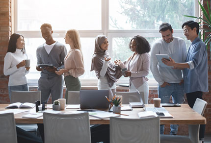 Business team standing by a meeting table and talking amongst each other.