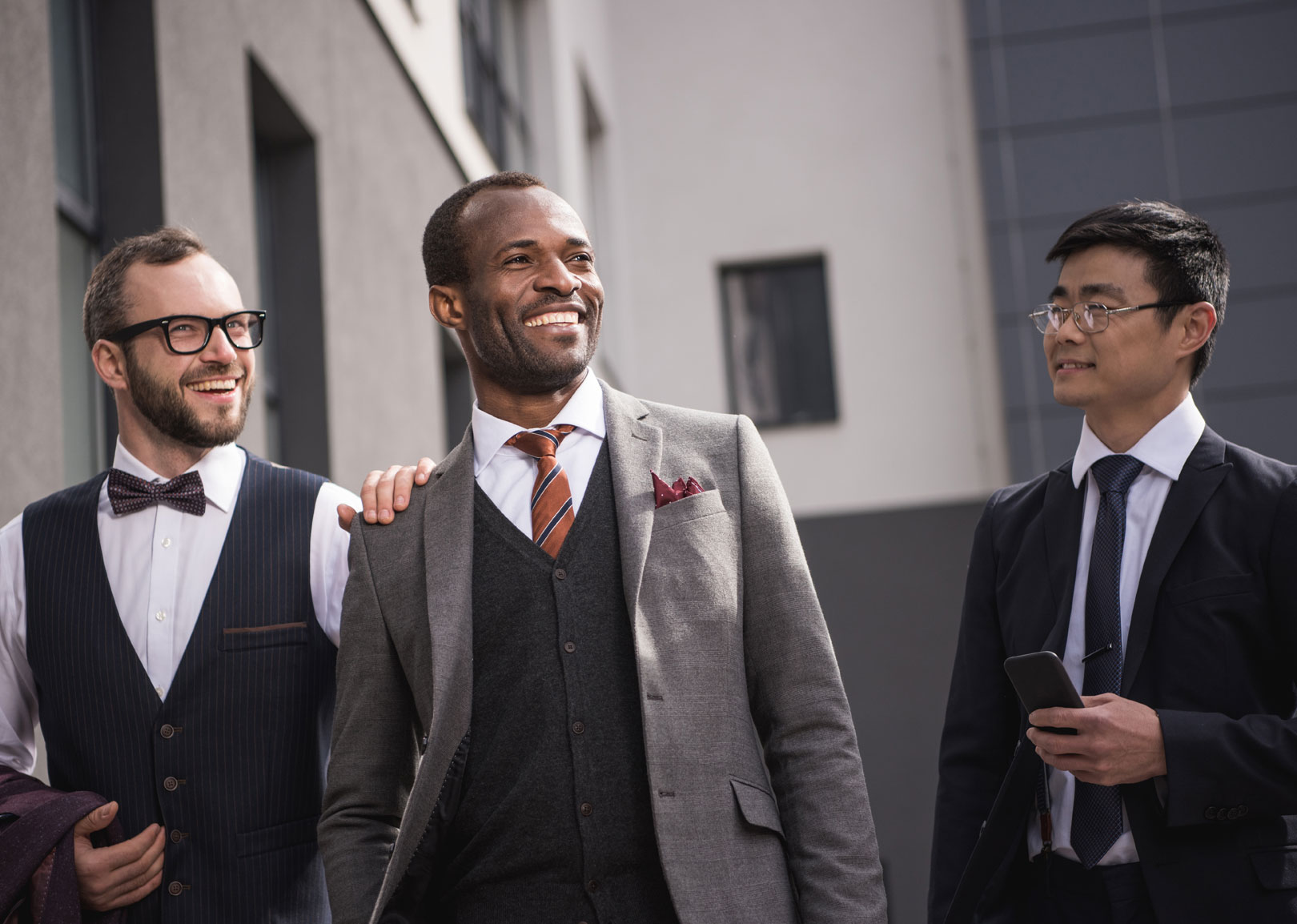 Trois hommes divers en tenue formelle, riant et discutant en marchant.